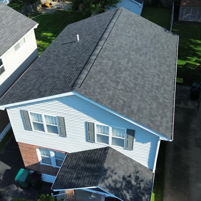 Finished charcoal shingle roof on a light blue home